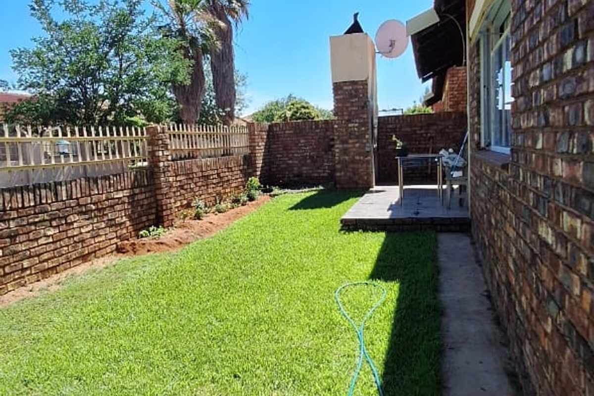 A private rear garden featuring a brick boundary wall, a small paved patio area, and a well-maintained lawn.
