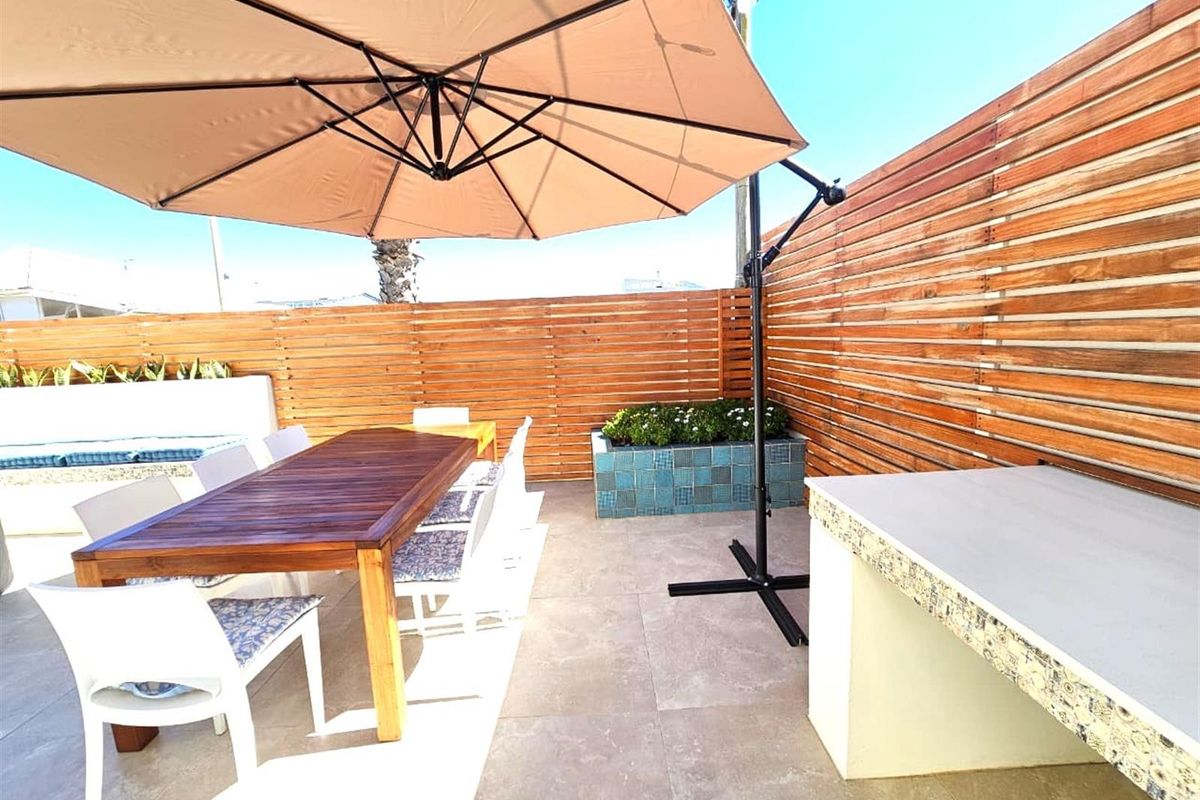 A private outdoor patio area featuring tiled flooring, a built-in stone-topped counter, and timber slat privacy fencing.