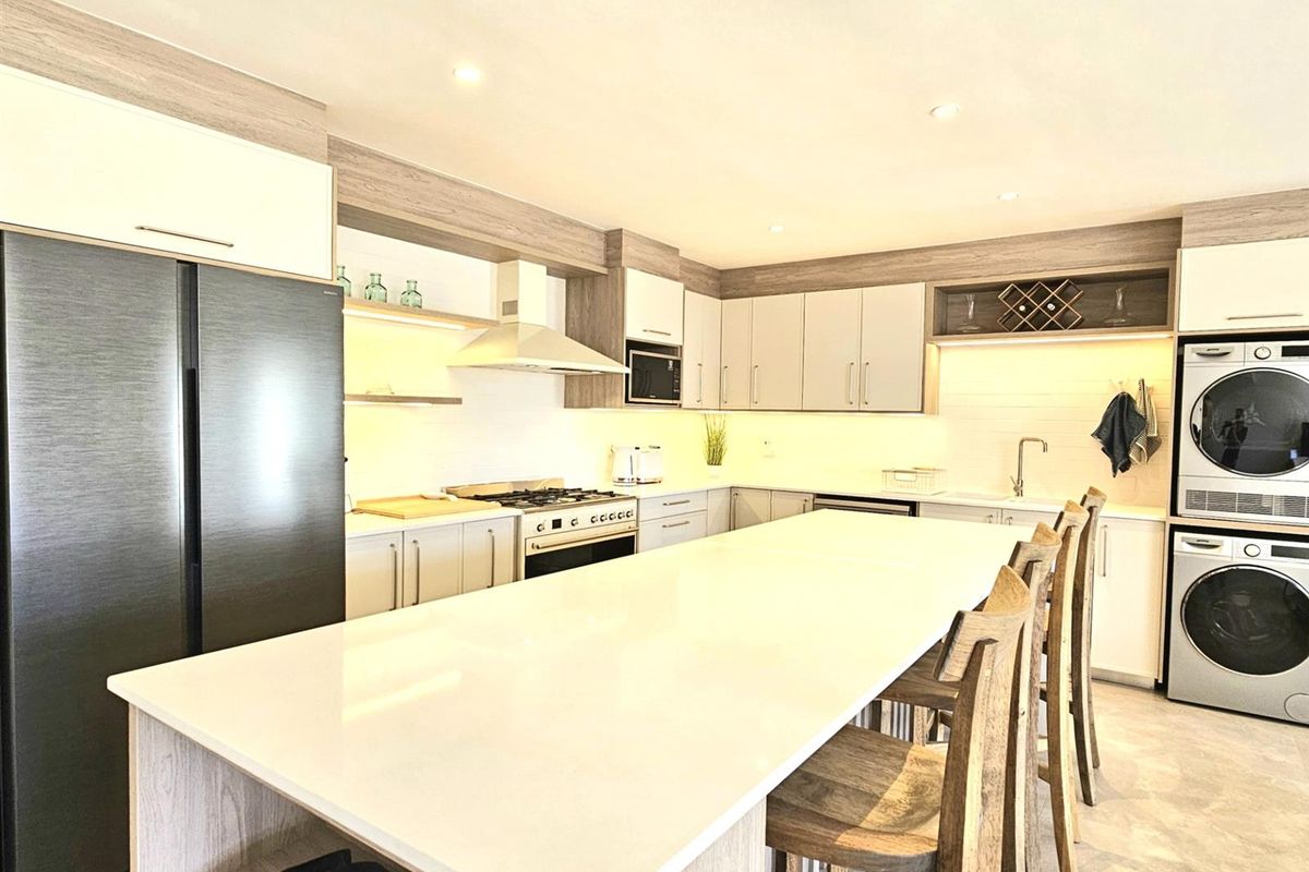 Modern kitchen featuring a large central island with stone countertop, integrated cabinetry, built-in oven, extractor fan, and dedicated laundry appliance space.