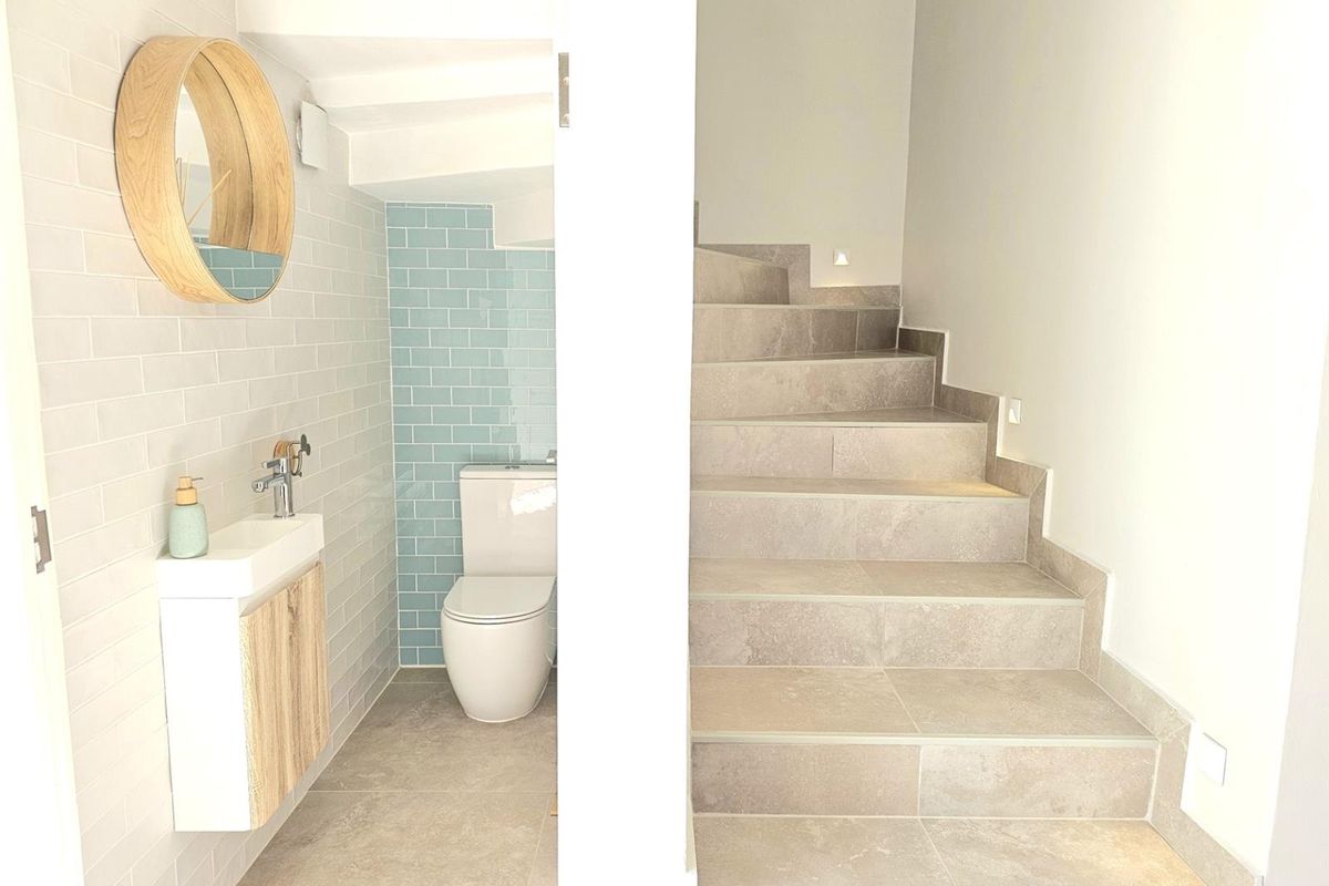 A modern bathroom featuring light blue subway tiles, a wall-mounted vanity, and a toilet, adjacent to a tiled staircase with integrated lighting.