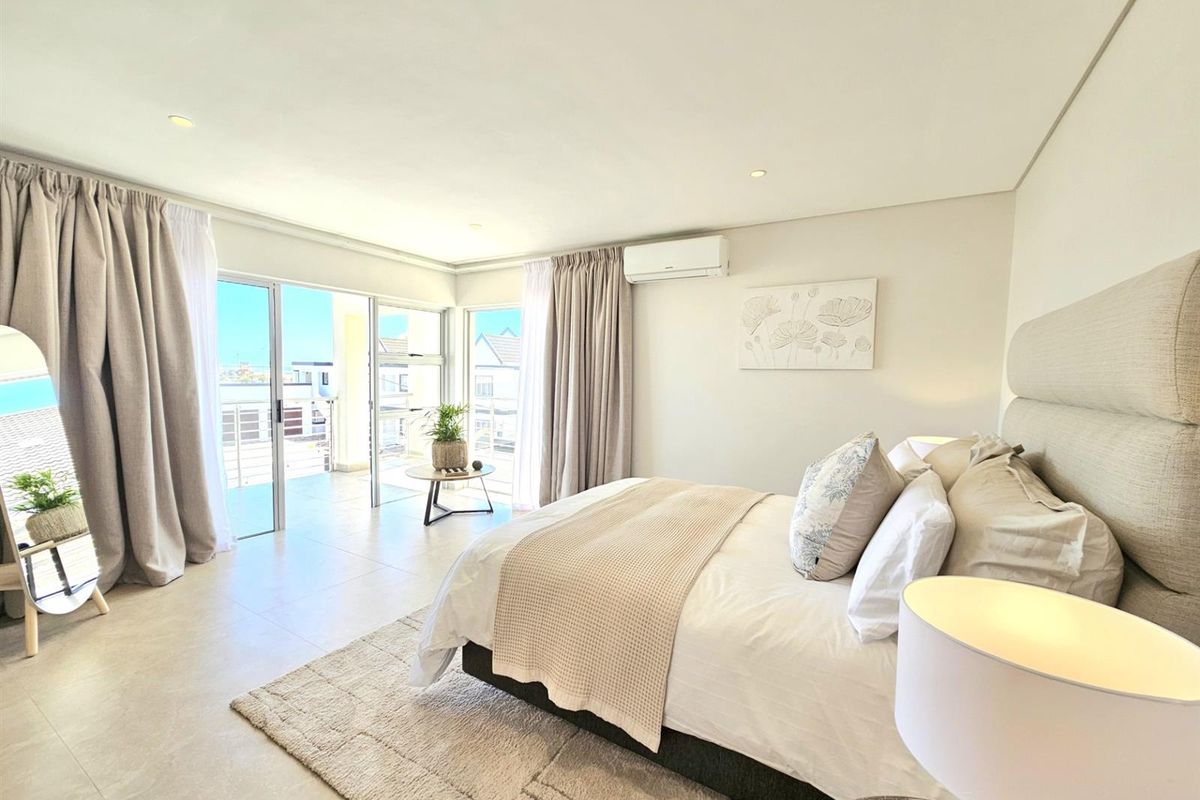Spacious bedroom featuring neutral tones, tiled flooring, recessed lighting, a wall-mounted air conditioning unit, and large sliding glass doors leading to a private balcony.