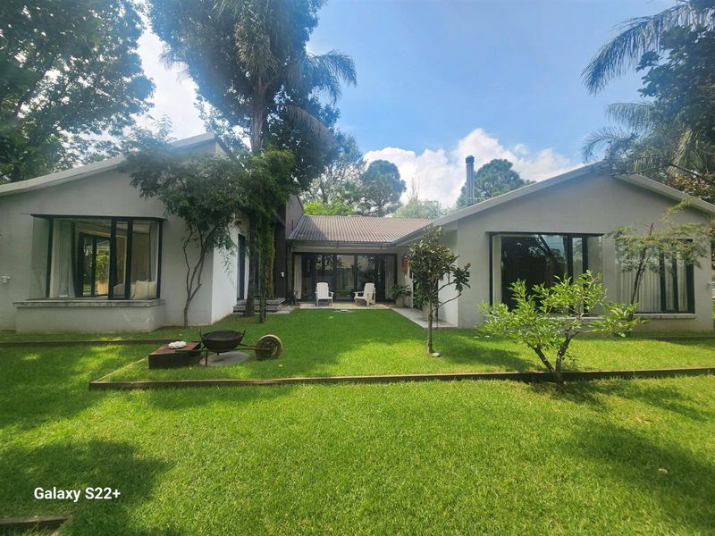 A well-maintained rear exterior view of the house featuring a spacious lawn, large windows, and sliding glass doors leading to the garden.