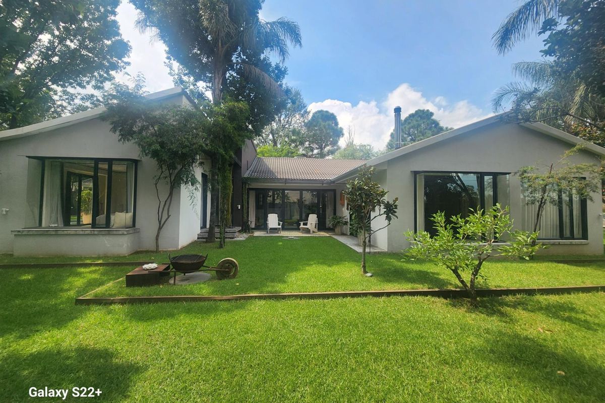 A well-maintained rear exterior view of the house featuring a spacious lawn, large windows, and sliding glass doors leading to the garden.