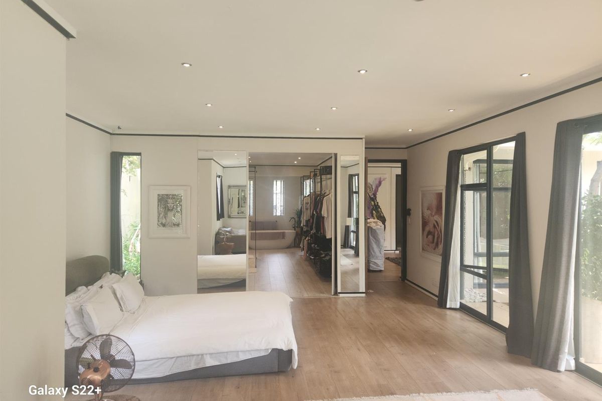 Spacious master bedroom featuring timber flooring, recessed lighting, and integrated wardrobe storage with mirrored doors, leading into an open-plan en-suite bathroom area.