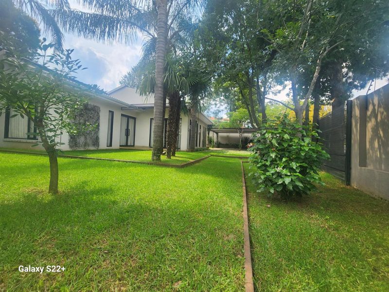 A well-maintained rear garden featuring lush green lawn, mature trees, and direct access to the home through large sliding glass doors.