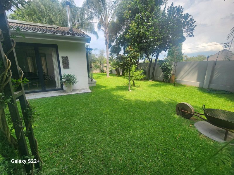 A view of the rear garden featuring a well-maintained lawn, perimeter wall, and access to the home via sliding glass doors.