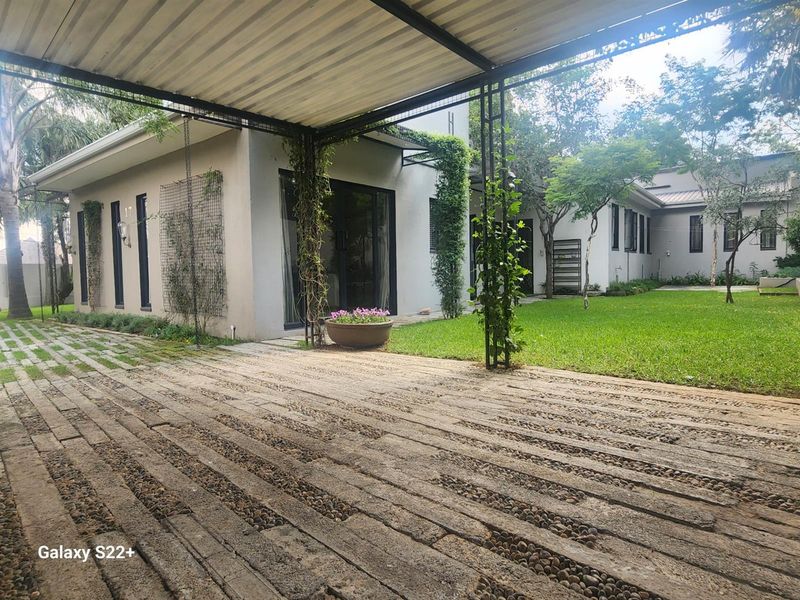A well-maintained rear exterior view featuring a covered patio area, paved driveway, and a lush green garden with established landscaping.