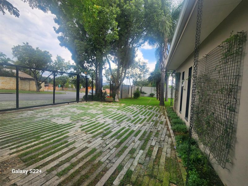 Front exterior view featuring a paved driveway, metal security gate, and established garden area with perimeter walling.