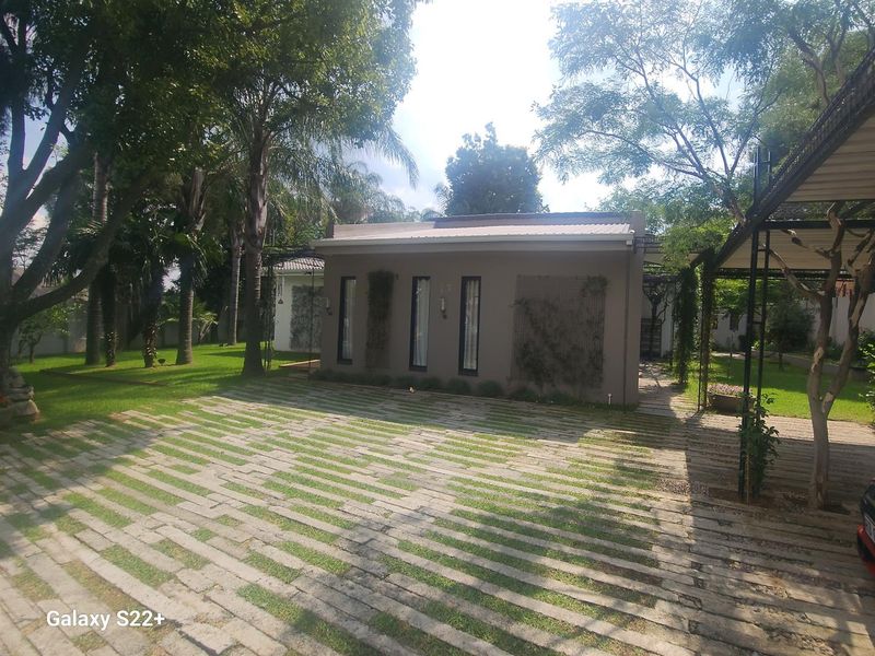 A well-maintained front exterior view featuring a paved driveway, covered carport, and established garden with mature trees surrounding the property.