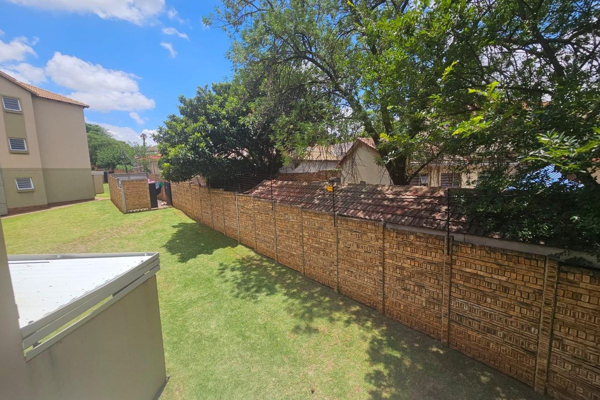 A view of the rear garden area featuring a well-maintained lawn, mature trees, and a secure brick boundary wall.