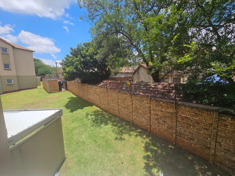 A view of the rear garden area featuring a well-maintained lawn, mature trees, and a secure brick boundary wall.