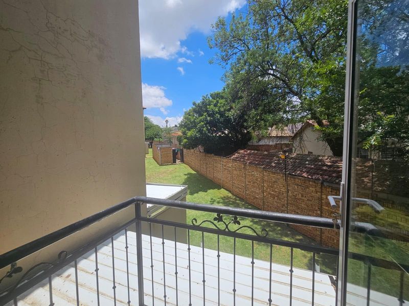 A balcony with a wrought iron balustrade overlooking a shared garden area and brick boundary wall.