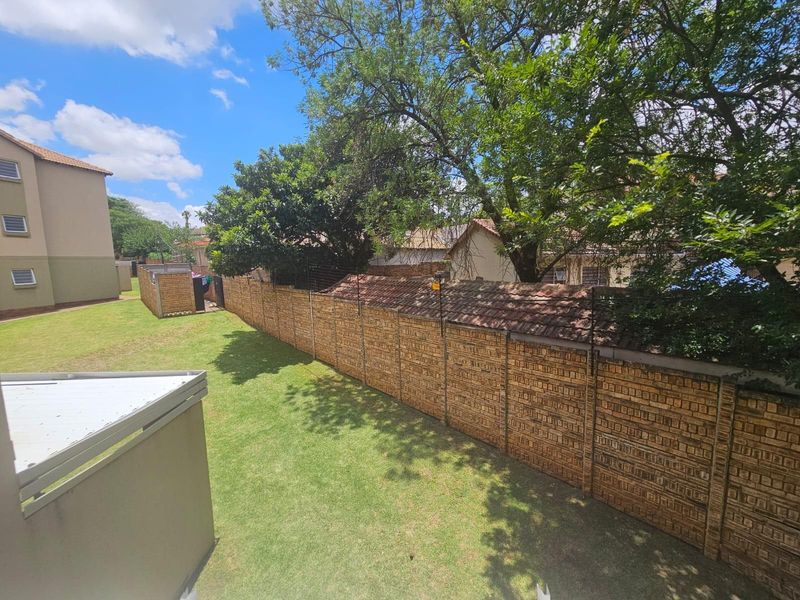 A view of the rear garden area featuring a well-maintained lawn, mature trees, and a secure brick boundary wall with electric fencing.