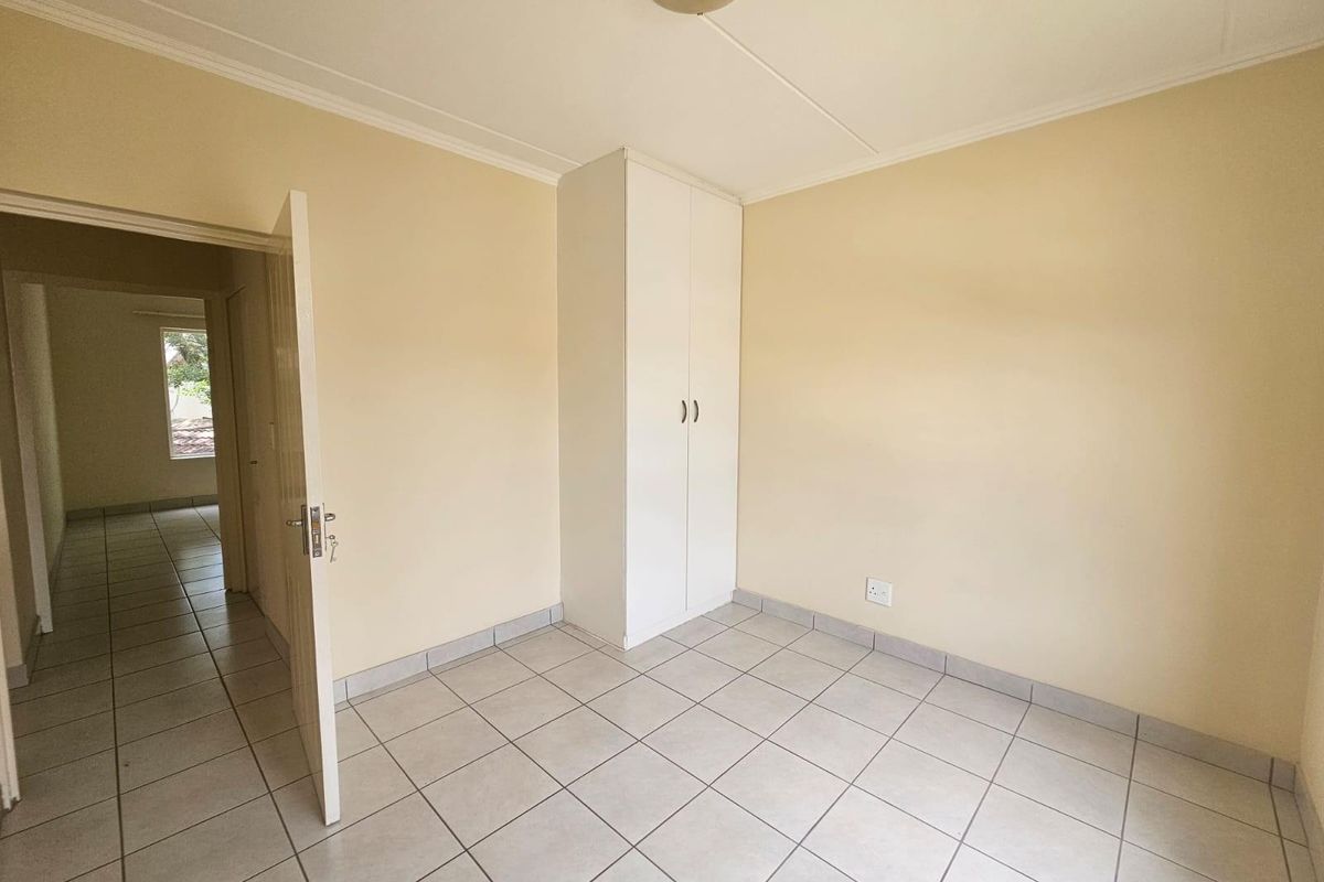 A clean, empty bedroom featuring neutral wall paint, tiled flooring, and a built-in wardrobe, offering a blank canvas for personalization.