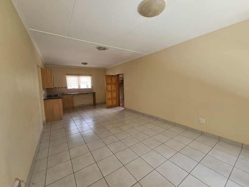 An empty open-plan living and kitchen area featuring tiled flooring, basic cabinetry, and neutral wall finishes, ready for renovation or staging.