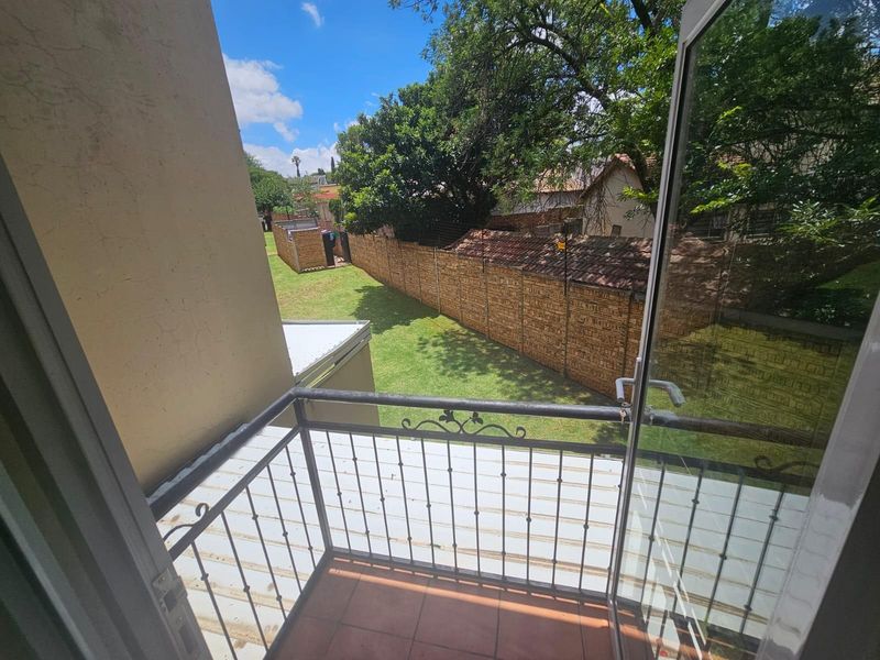 A small balcony with a wrought iron balustrade and tiled flooring, overlooking a private garden area with a brick boundary wall.