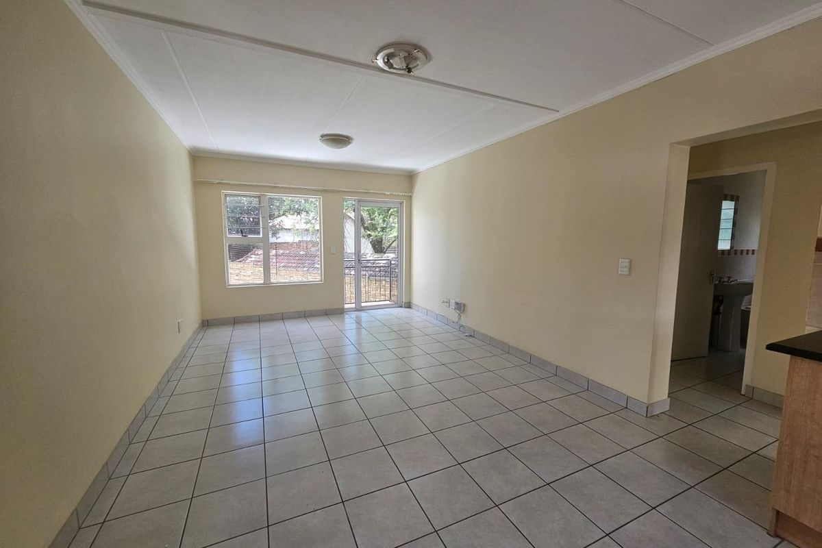 An empty, open-plan living area featuring neutral tiled flooring, large windows, and a sliding glass door providing access to the exterior.