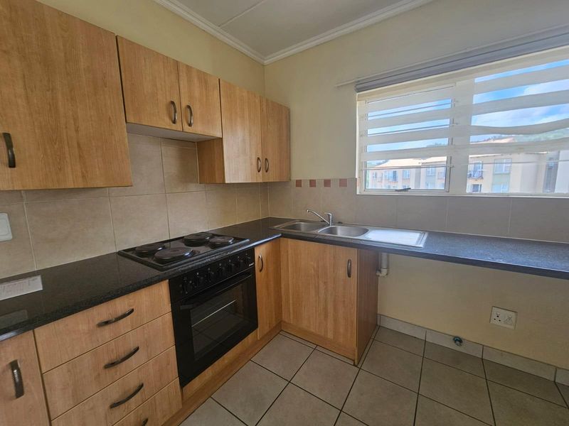 A functional kitchen featuring wood-finish cabinetry, dark laminate countertops, a built-in oven and hob, and tiled flooring with a double bowl sink.