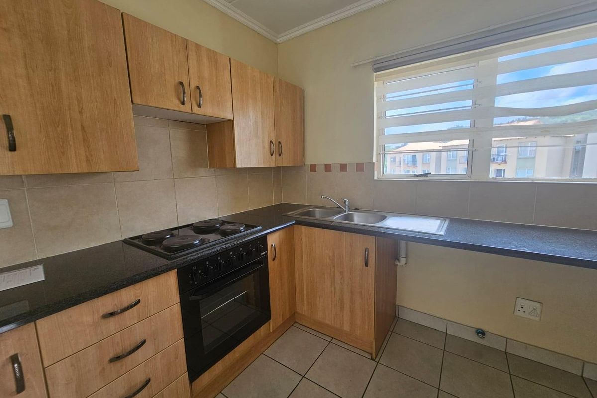 A functional kitchen featuring wood-finish cabinetry, dark laminate countertops, a built-in oven and hob, and tiled flooring with a double bowl sink.