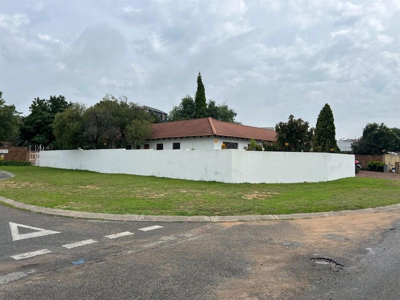 Street-level view of the property featuring a white perimeter wall, tiled roof, and established garden area.