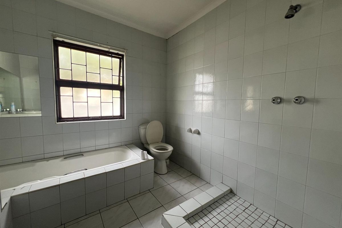 A functional bathroom featuring a built-in bathtub, a separate tiled shower area, and a toilet, finished with white wall and floor tiles.