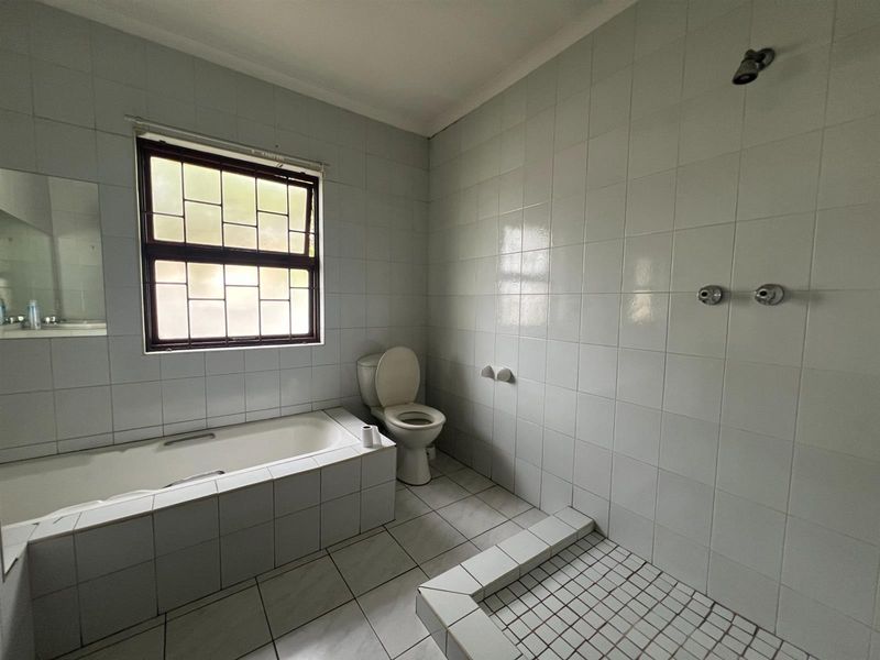A functional bathroom featuring a built-in bathtub, a separate tiled shower area, and a toilet, finished with white wall and floor tiles.