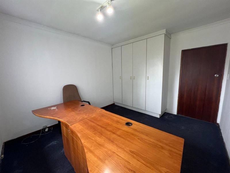 A functional office space featuring built-in storage cupboards, dark carpeting, and overhead track lighting, suitable for a professional workspace.