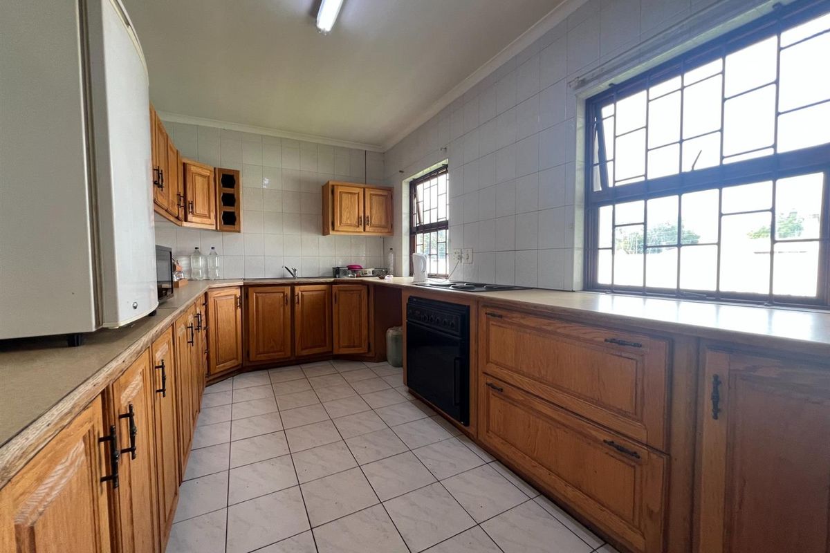 A functional kitchen featuring wooden cabinetry, built-in oven, hob, and tiled finishes, offering a practical workspace with natural light from large windows.