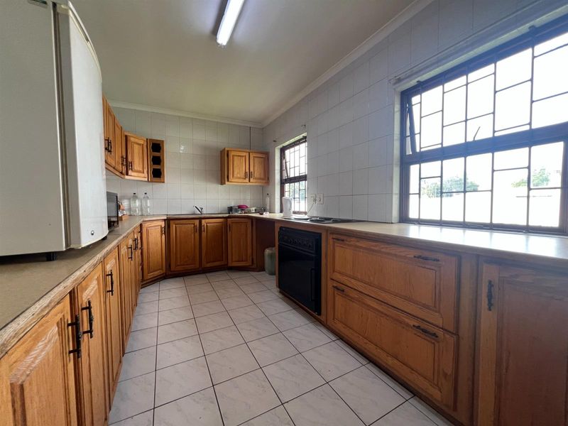 A functional kitchen featuring wooden cabinetry, built-in oven, hob, and tiled finishes, offering a practical workspace with natural light from large windows.