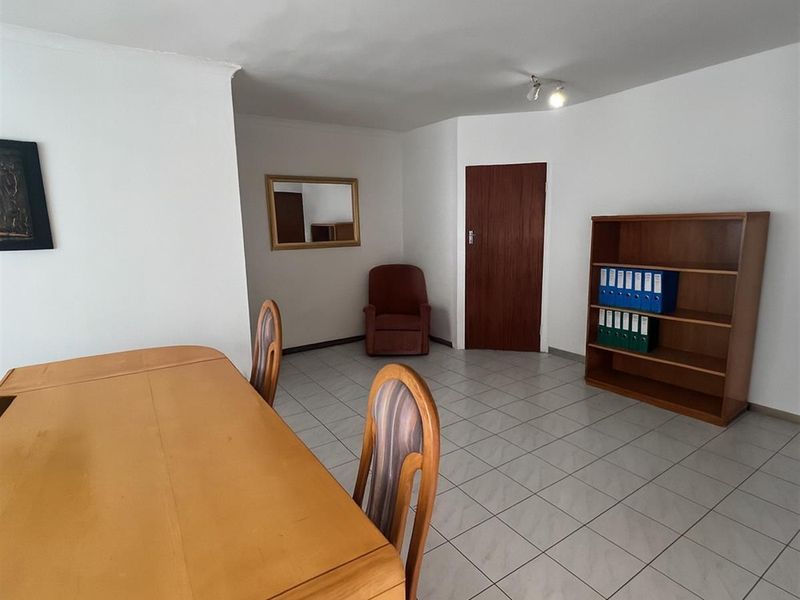 A functional office space featuring neutral tiled flooring, a solid wooden door, and overhead spotlighting, providing a clean and professional work environment.