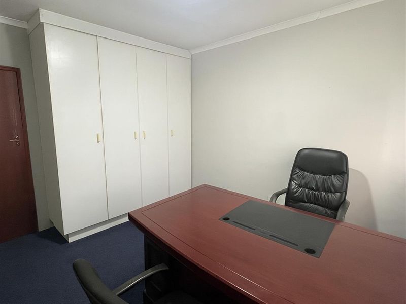 A functional office space featuring built-in storage cupboards, blue carpeting, and neutral wall finishes, suitable for a professional work environment.