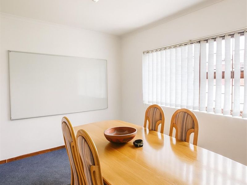 A functional office space featuring carpet flooring, a wall-mounted whiteboard, and vertical blinds, providing a practical environment for meetings or administrative tasks.