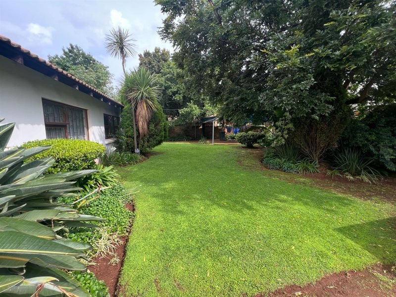 A well-maintained rear garden featuring a lush lawn, mature trees, and established landscaping, bordered by a brick wall and the rear elevation of the building.