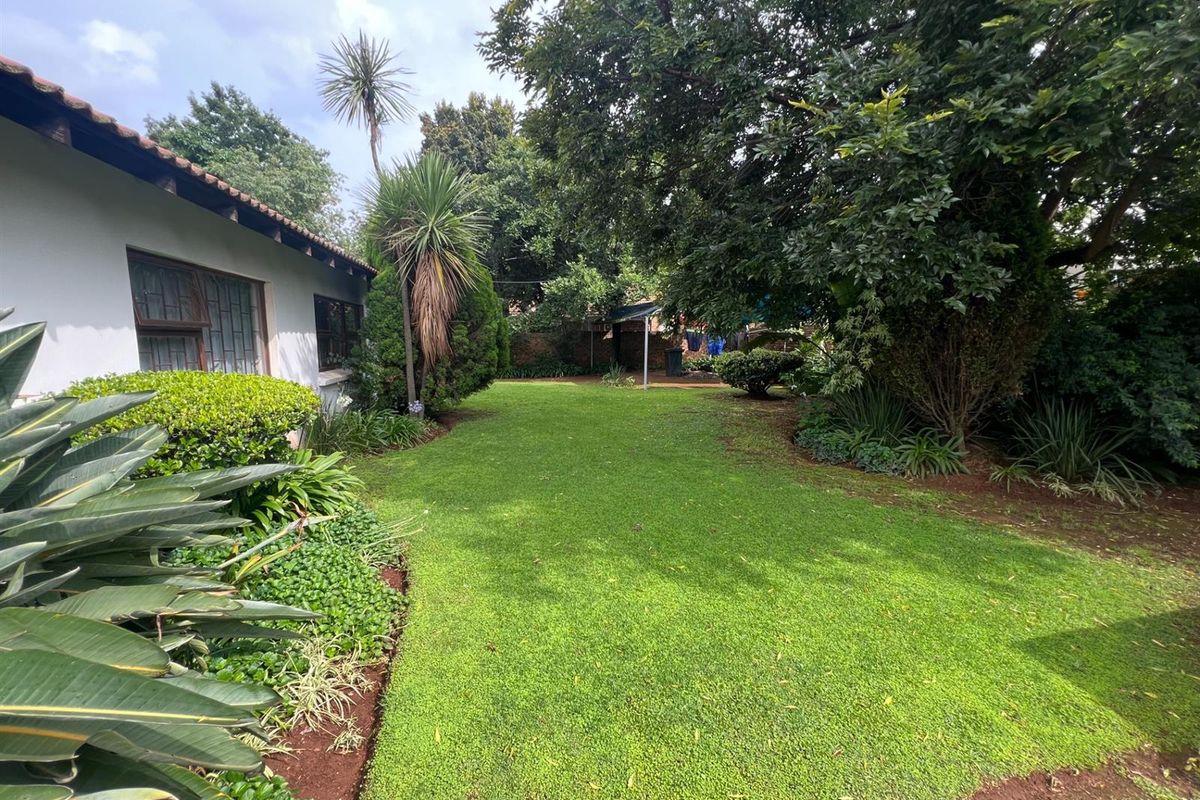 A well-maintained rear garden featuring a lush lawn, mature trees, and established landscaping, bordered by a brick wall and the rear elevation of the building.