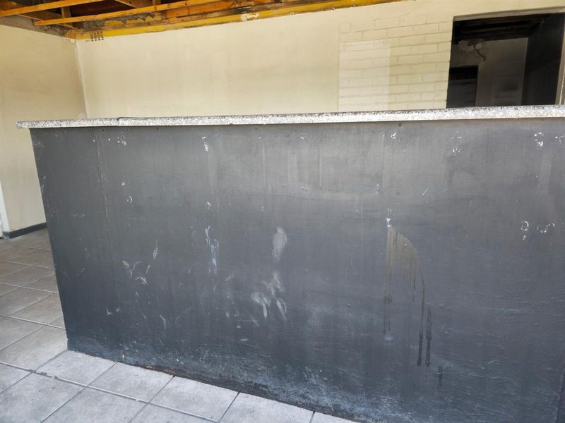 A vacant commercial bar area featuring a built-in counter with a granite top, requiring significant renovation and finishing to the walls and ceiling.