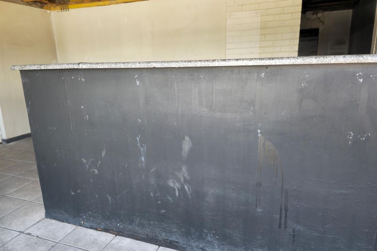 A vacant commercial bar area featuring a built-in counter with a granite top, requiring significant renovation and finishing to the walls and ceiling.