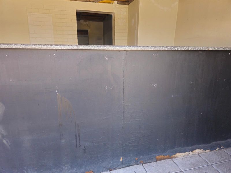 A commercial kitchen service counter featuring a stone top, currently in need of cosmetic repairs and finishing to the surrounding wall and base.