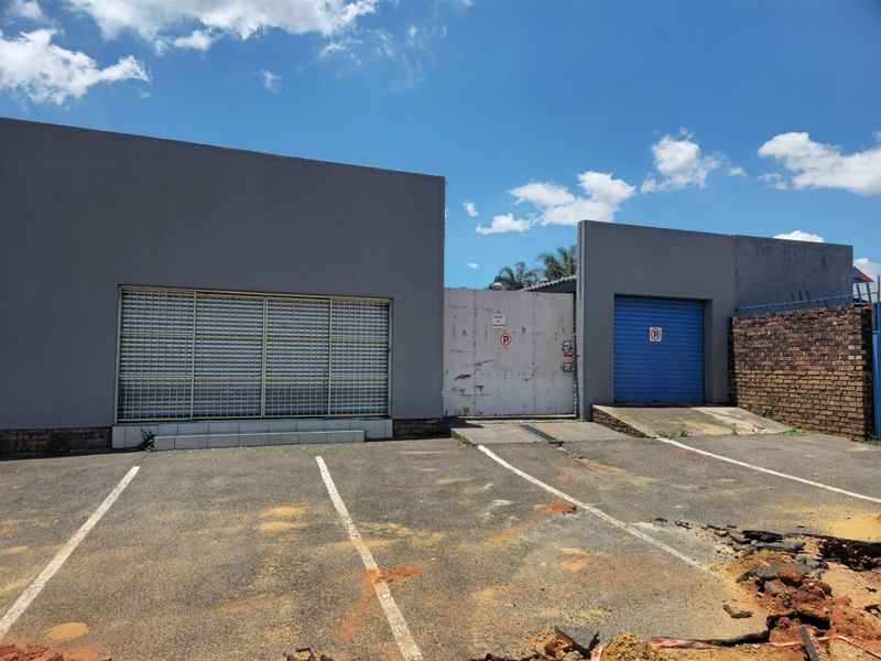 Commercial property exterior featuring a paved parking area, security roller shutters, and a gated entrance with a roller garage door.
