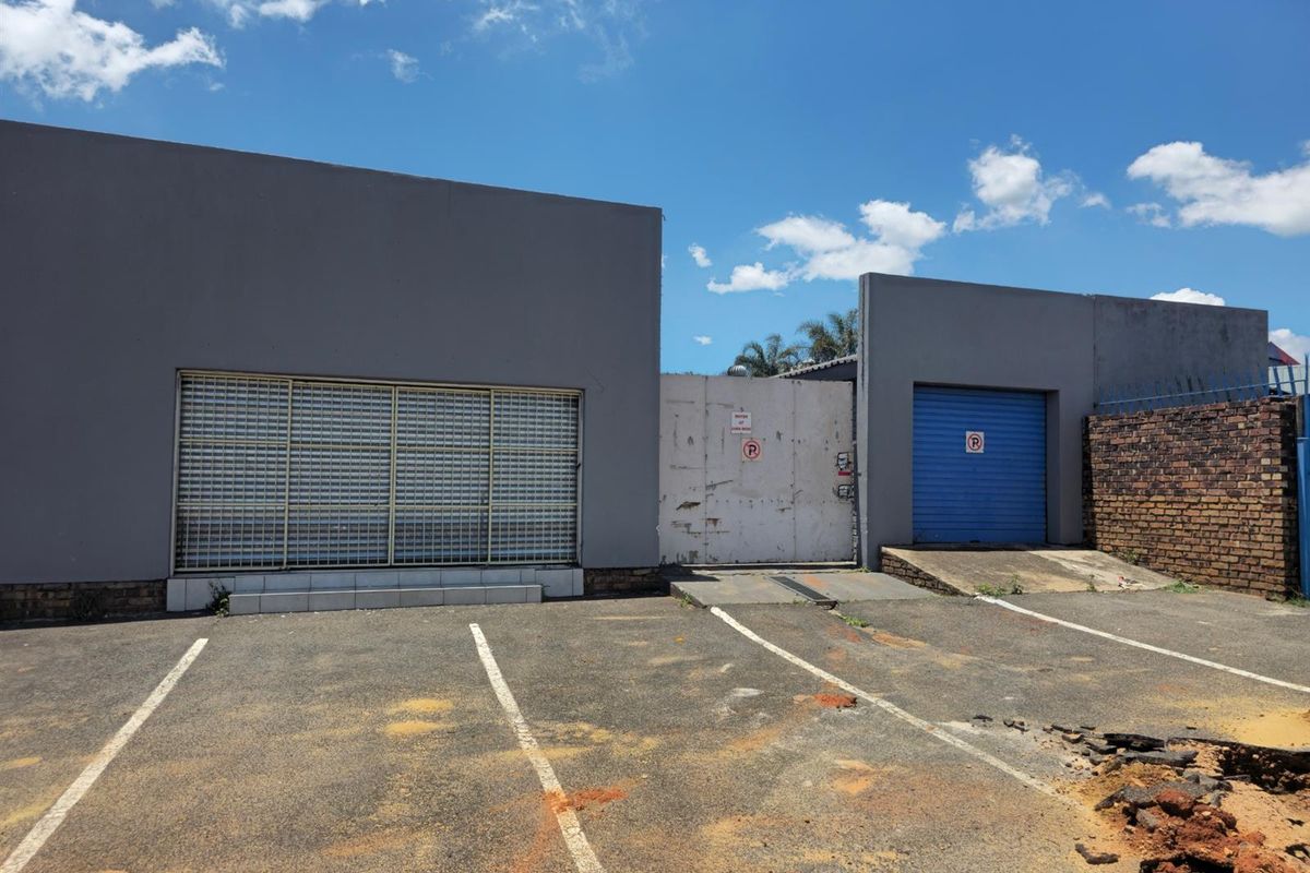 Commercial property exterior featuring a paved parking area, security roller shutters, and a gated entrance with a roller garage door.