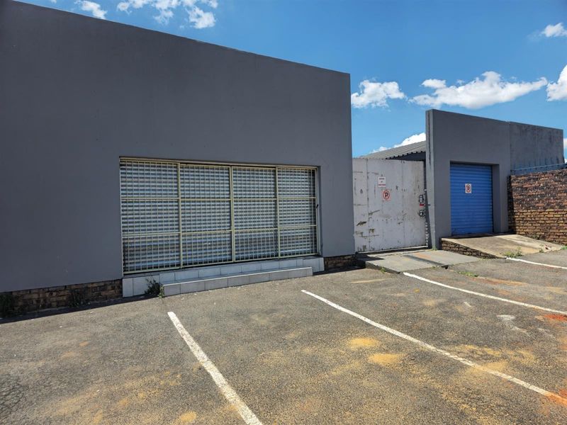 Commercial property exterior featuring a secure roller shutter entrance, paved parking area, and gated access with a blue metal garage door.