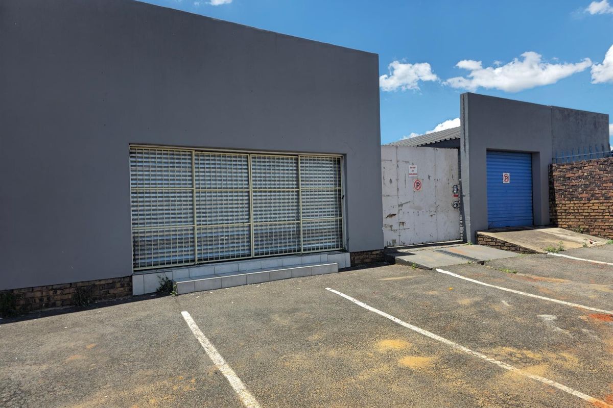 Commercial property exterior featuring a secure roller shutter entrance, paved parking area, and gated access with a blue metal garage door.