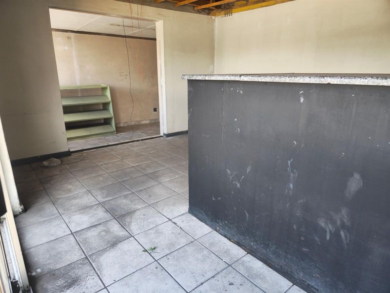 Open-plan commercial space featuring tiled flooring, a built-in service counter with granite top, and exposed ceiling structure, currently in need of renovation.