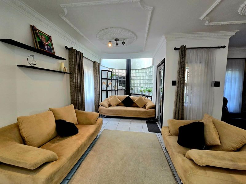 A living room featuring decorative ceiling cornices, a central ceiling rose, and a distinctive glass block feature wall providing natural light.