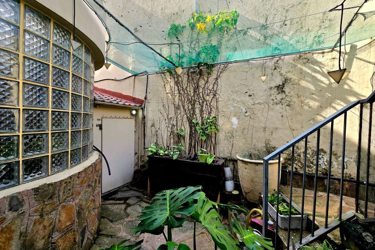 A small, enclosed outdoor courtyard featuring a curved glass block wall, stone paving, and a metal staircase leading to an upper level.