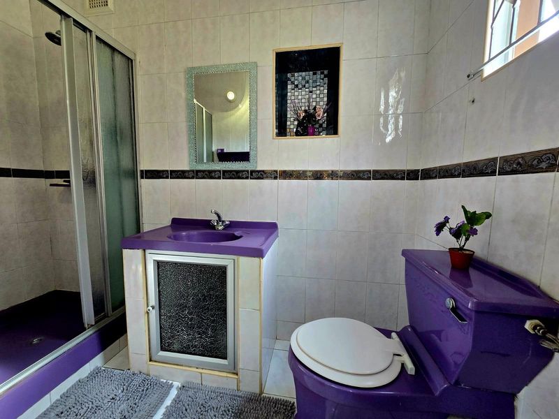 A compact bathroom featuring a shower enclosure, a purple vanity basin, and a matching purple toilet with tiled walls.