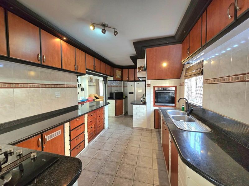 Spacious kitchen featuring dark granite countertops, wood-finish cabinetry, built-in oven, and tiled flooring with a functional layout.