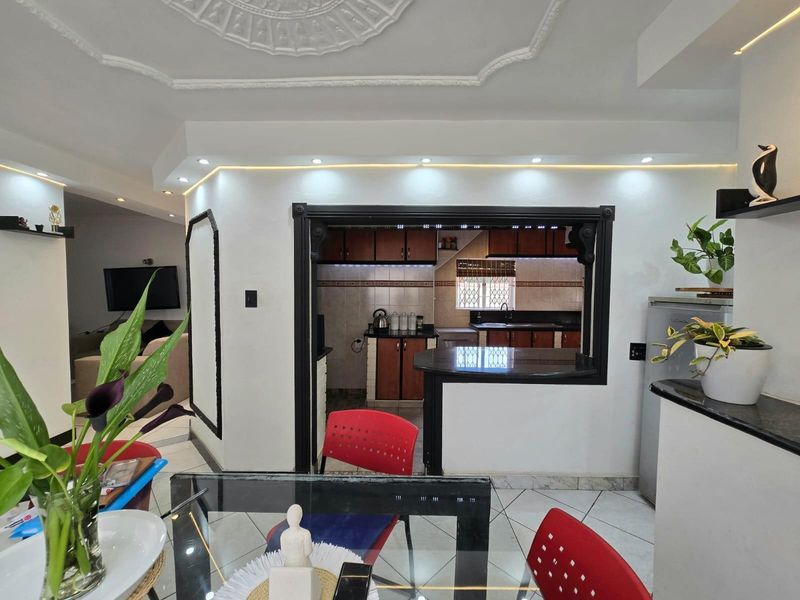 Open plan living and dining area featuring a pass-through kitchen with dark cabinetry, granite countertops, and recessed ceiling lighting with decorative molding.