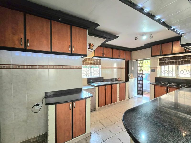 A functional kitchen featuring dark granite countertops, wood-finish cabinetry, tiled splashbacks, and a breakfast bar area with direct access to the exterior.