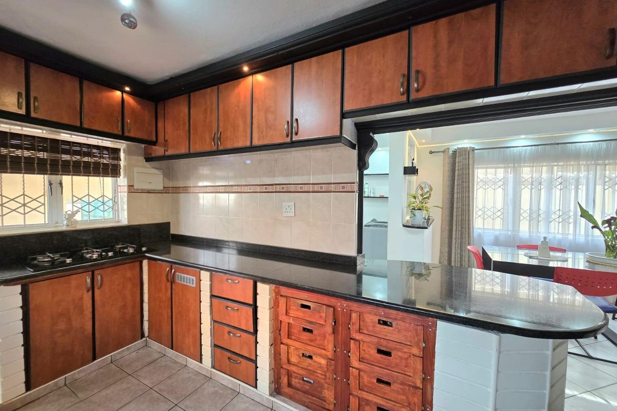 A functional kitchen featuring dark granite countertops, wooden cabinetry, a built-in gas hob, and a breakfast bar overlooking the adjacent living area.