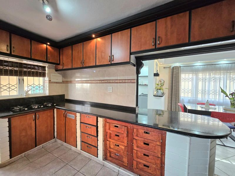 A functional kitchen featuring dark granite countertops, wooden cabinetry, a built-in gas hob, and a breakfast bar overlooking the adjacent living area.